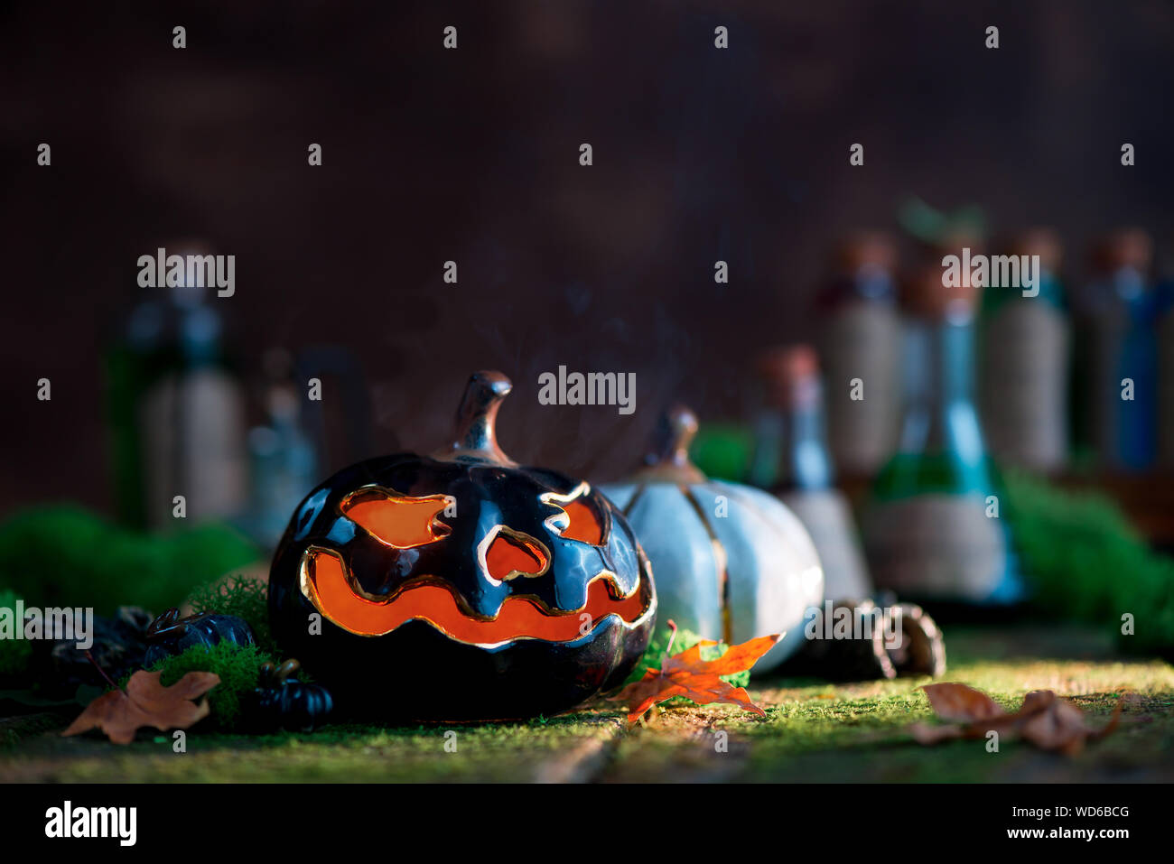 Ceramic pumpkin with glowing eyes on a background with moss and fallen leaves with copy space. Halloween still life Stock Photo