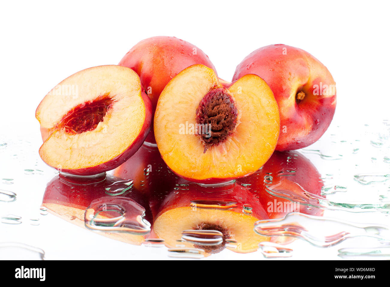 Whole peaches and two halves of a peach with a stone inside on a white mirror background with reflection in water drops close up isolated Stock Photo