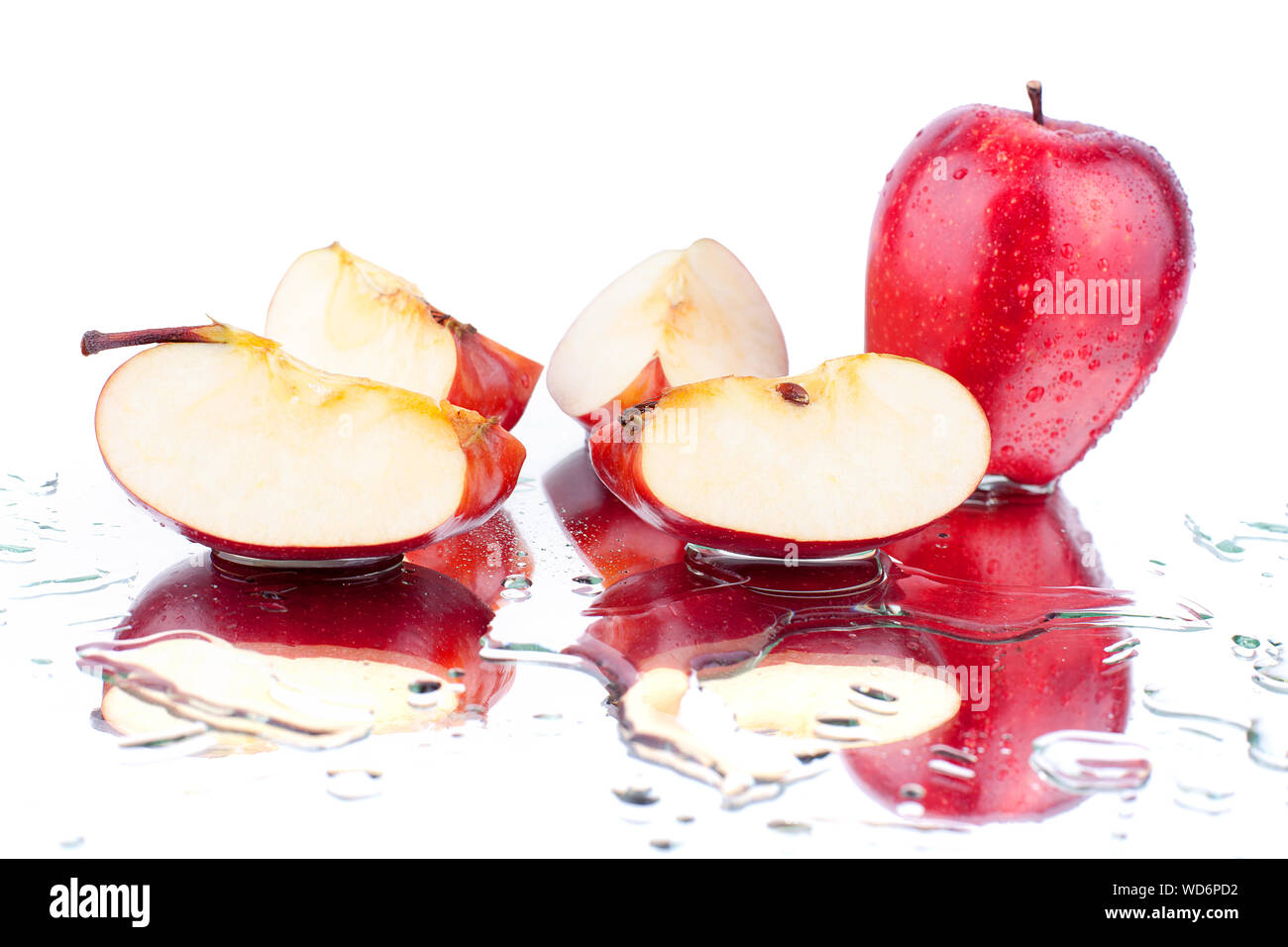 Whole red apple and apple sliced on quarters on white mirror background with water drops and reflection isolated close up Stock Photo