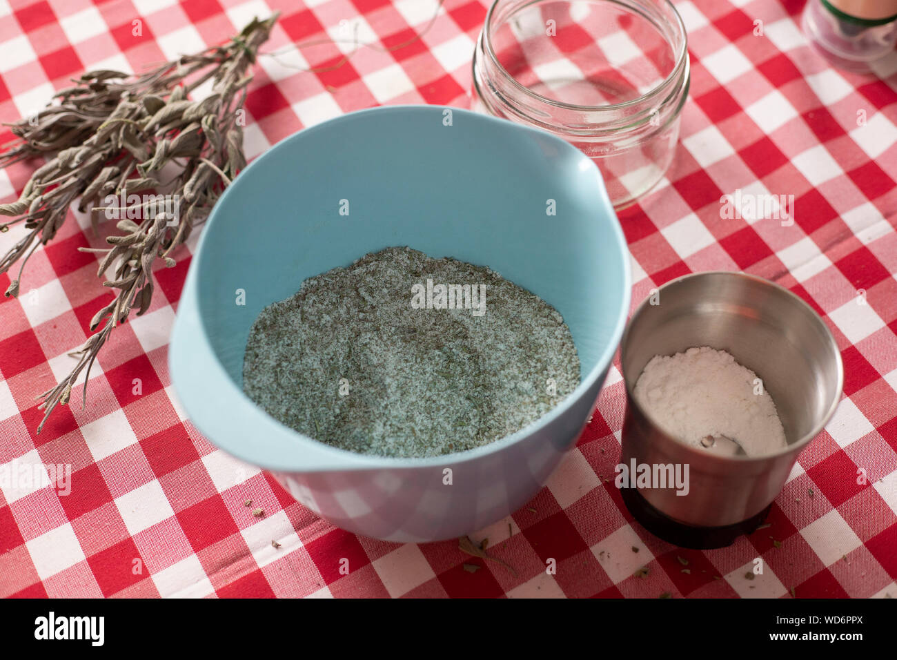 Blue bowl containing aromatics herbs - like dried sage and rosemary - mixed with sea salt using a blender, an homemade seasoning for everyday cooking. Stock Photo