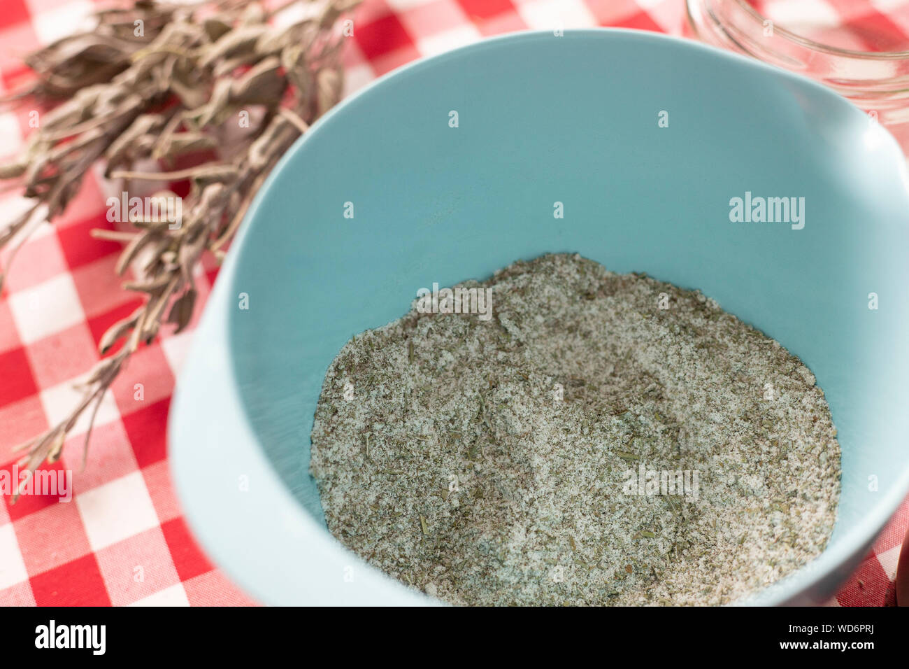 Blue bowl containing aromatics herbs - like dried sage and rosemary - mixed with sea salt using a blender, an homemade seasoning for everyday cooking. Stock Photo
