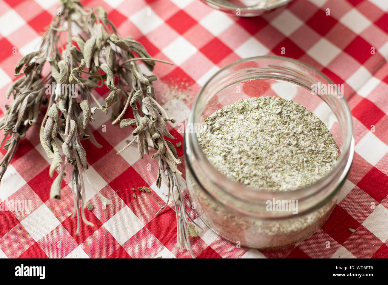 Glass vase containing aromatics herbs - like dried sage and rosemary - mixed with sea salt using a blender, an homemade seasoning for everyday cooking Stock Photo