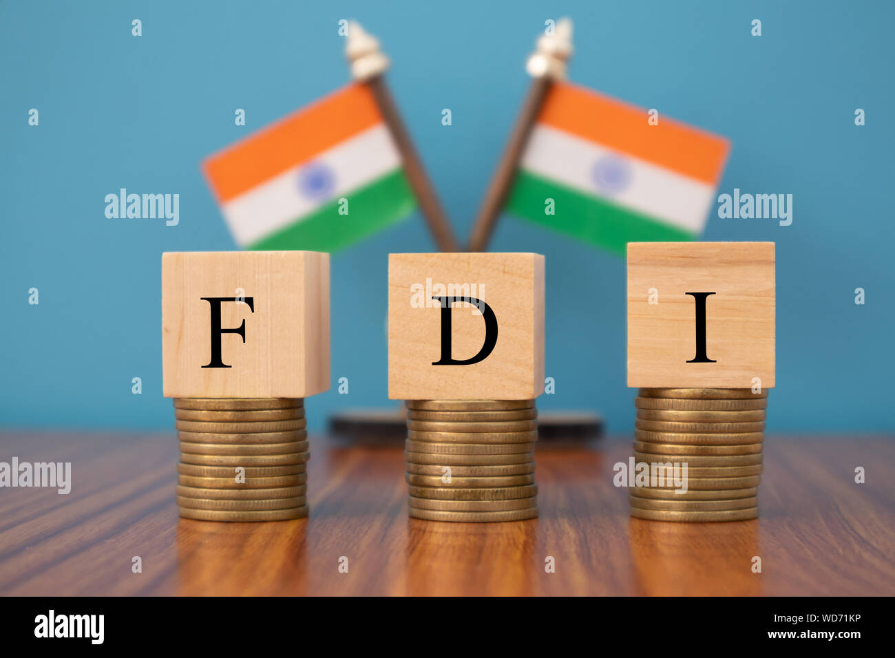 Concept of FDI or foreign Direct Investment on India in wooden block letters on stack of coins with Indian Flag as a background. Stock Photo