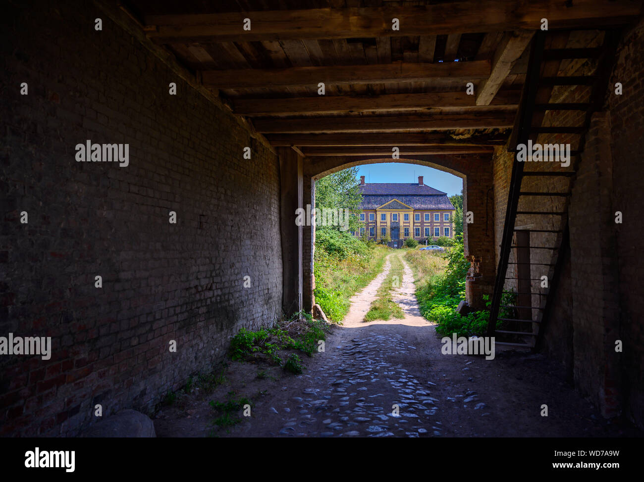 Johannstorf, Germany. 28th Aug, 2019. The only baroque moated castle in Mecklenburg-Vorpommern, the Gutshof Johannstorf, can be seen through the dilapidated gate house. The castle known from the film 'The White Ribbon' has stood empty for decades and has now been renovated by a private investor for six years. Credit: Jens Büttner/dpa-Zentralbild/dpa/Alamy Live News Stock Photo