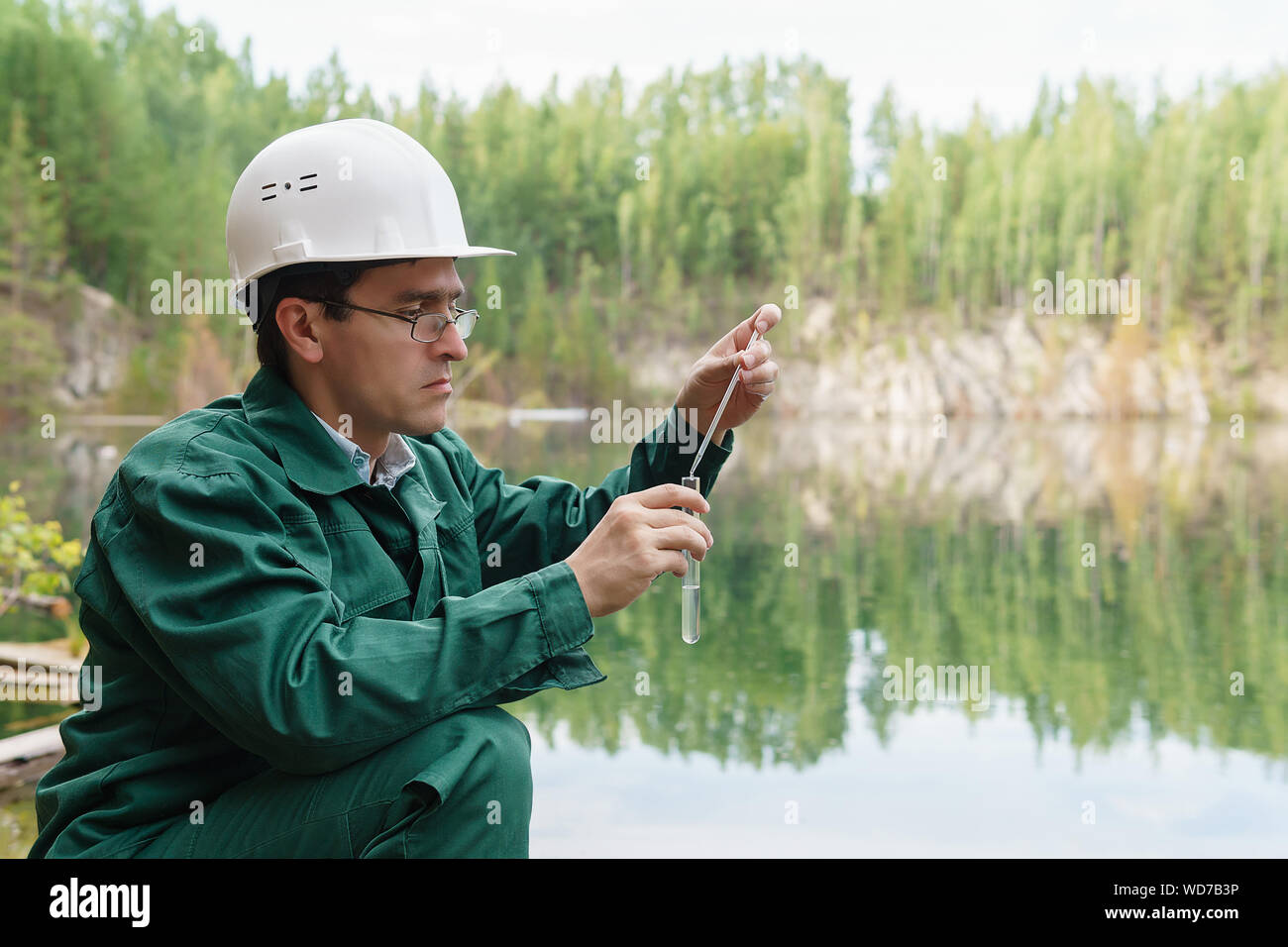 industrial ecologist or chemist takes a sample of water from lake at the site of a flooded quarry Stock Photo