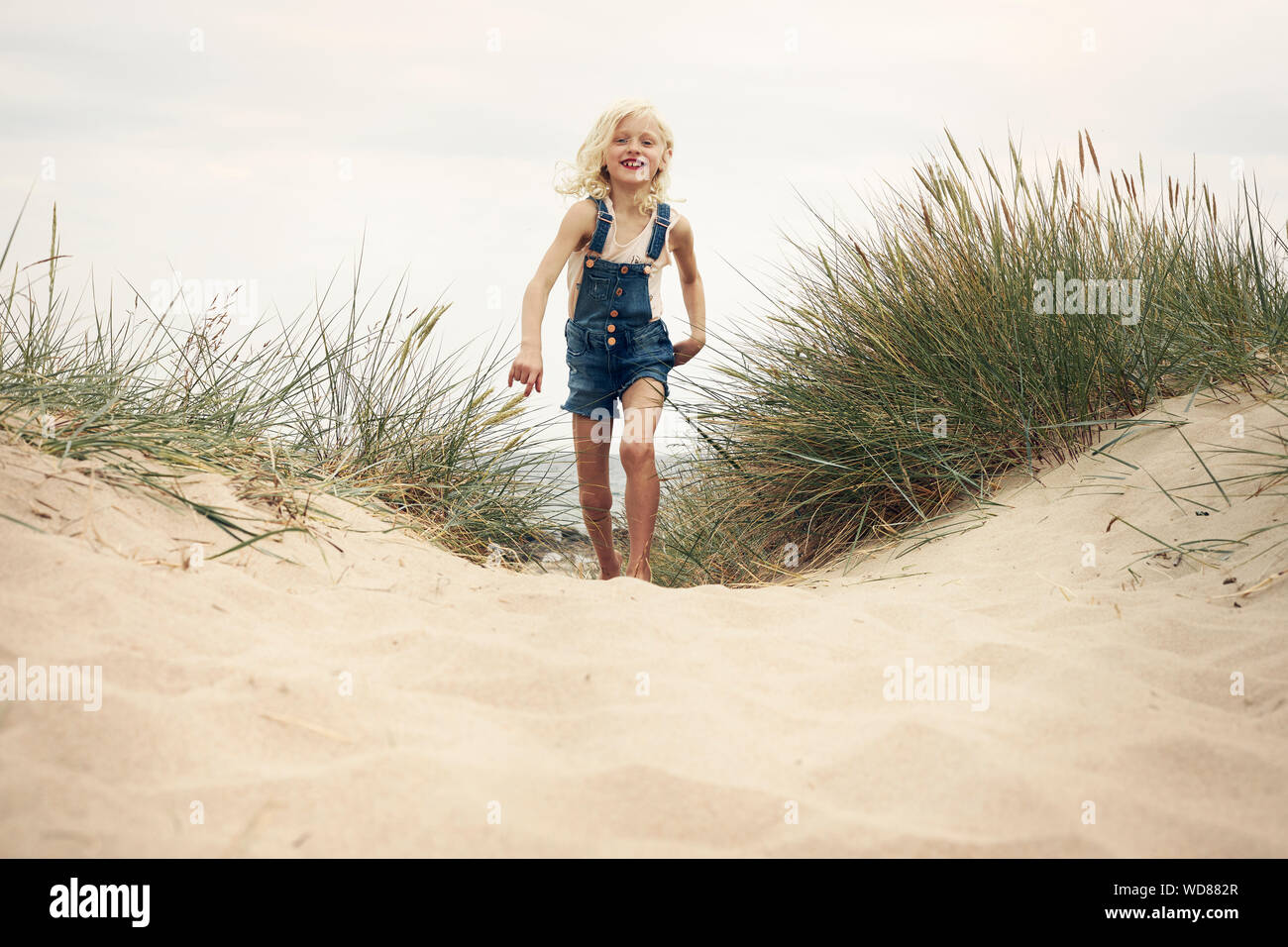Girl wearing denim overalls walking on sand dune Stock Photo