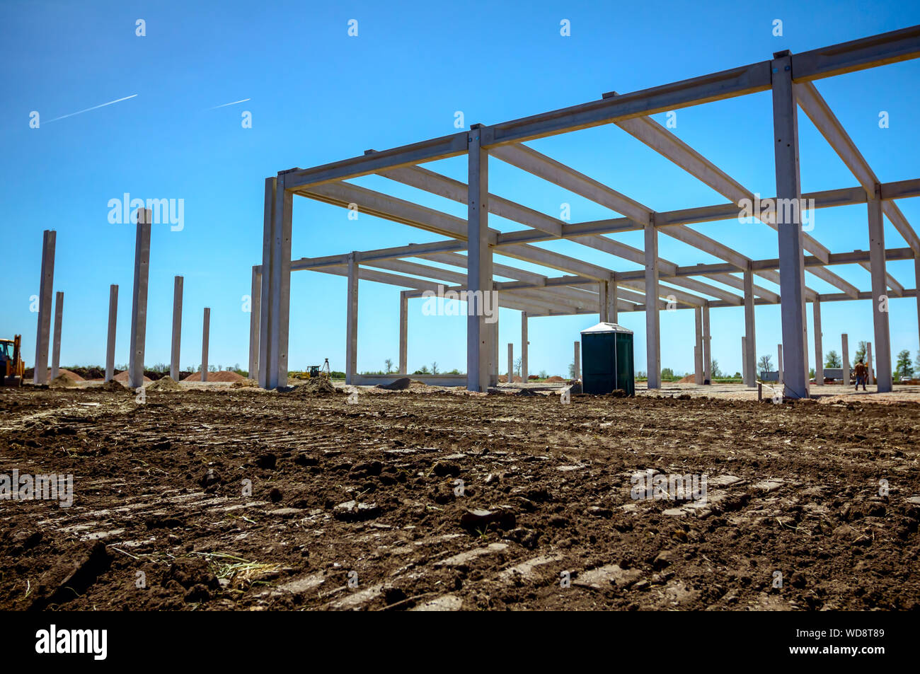 Concrete skeleton of unfinished new edifice and public lavatory for workers is placed at construction site. Stock Photo