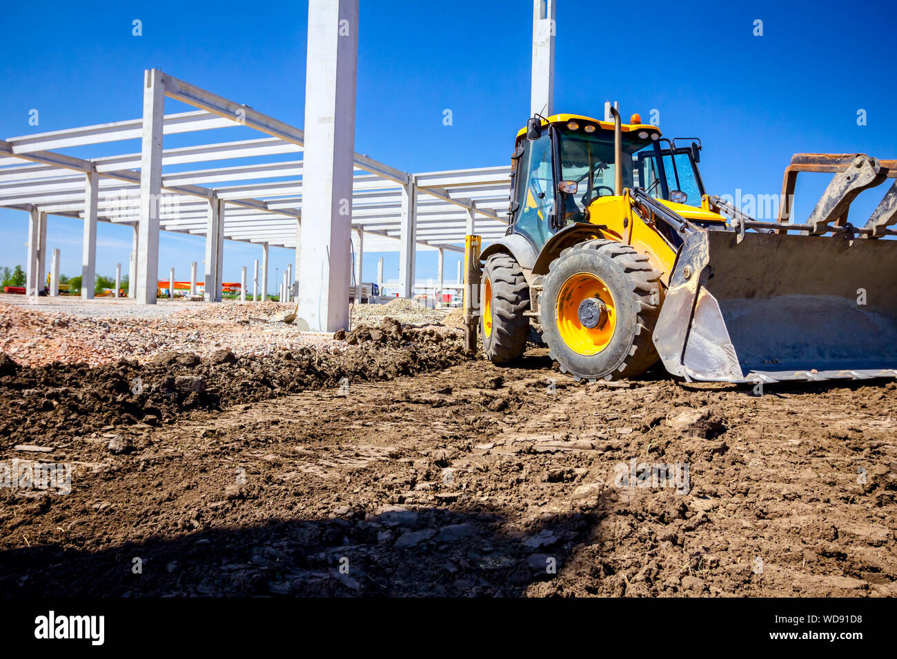 Excavator's front tool, bucket, blade, tall concrete pillars are behind at building site. Stock Photo