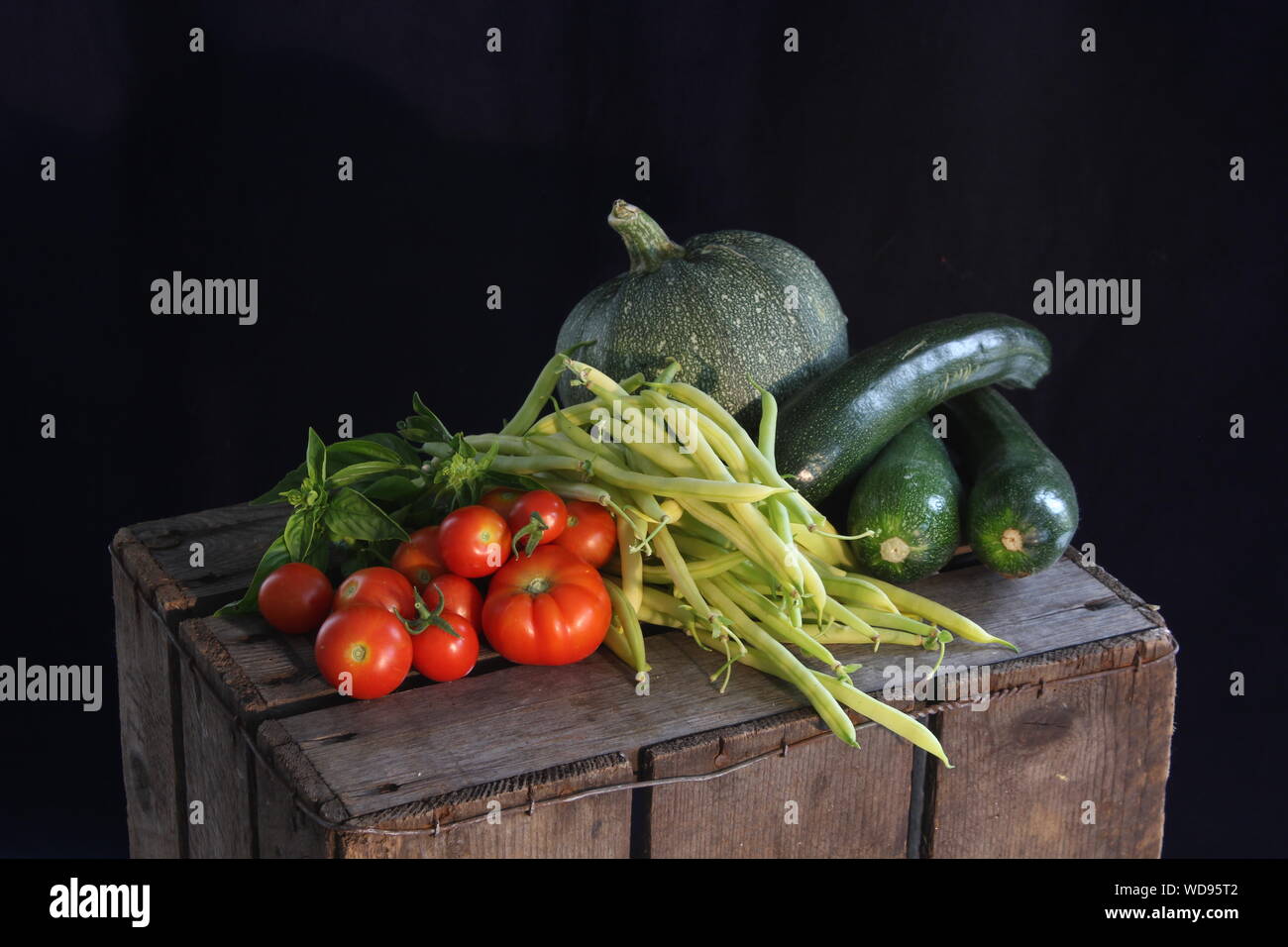 A still life of homegrown vegetables, green beans, courgettes, round courgettes, basil and tomatoes Stock Photo