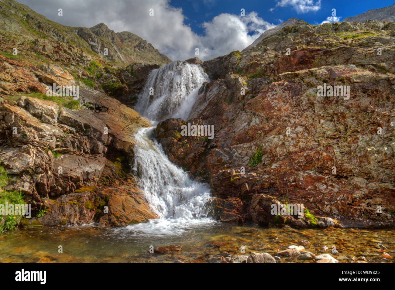 Small waterfall over red colored rocks and boulders, splashing in a small lake Stock Photo