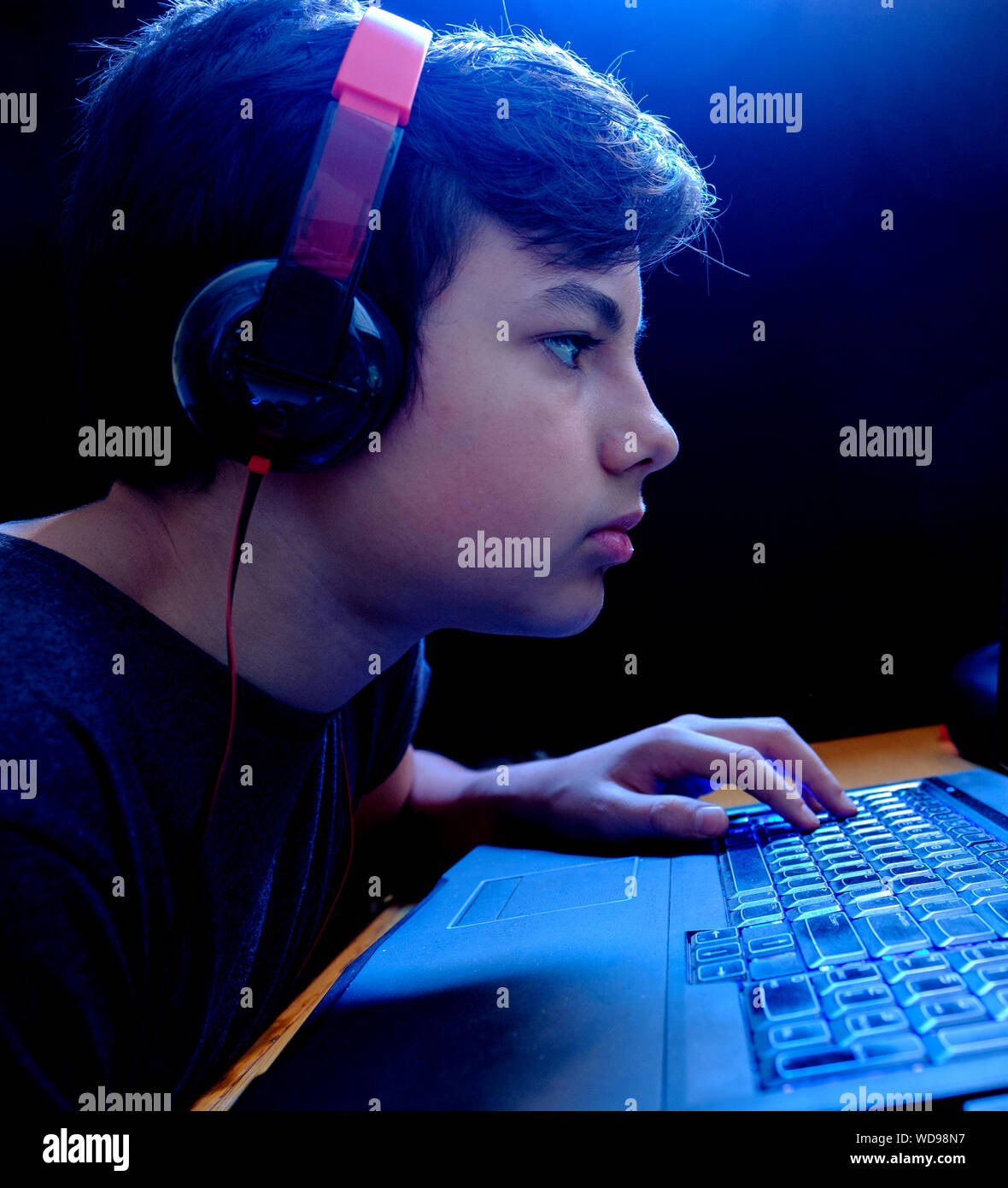 Antisocial, addictive behaviour, under aged, teenager boy gaming on his Laptop with his earphones on, isolated on a black background. Stock Photo