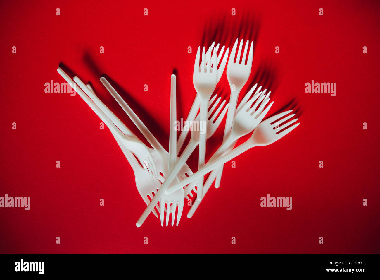 A lot of plastic forks on a red background. The concept of environmental problems, environmental pollution by plastic waste. Top view, close up. Stock Photo