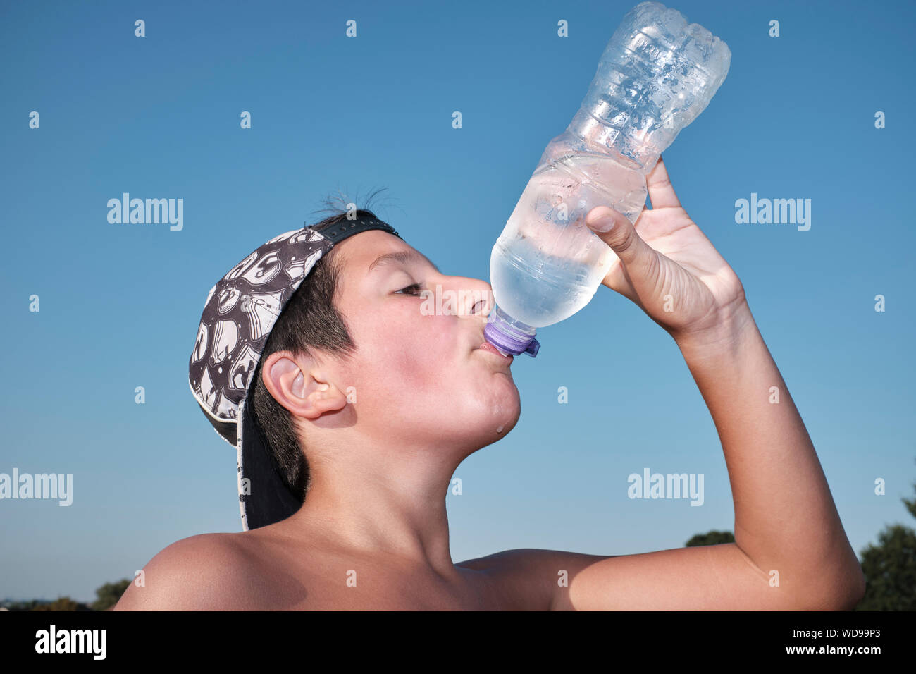 Boy, 11-12 years old, driks ice cold water from plastic bottle on a hot summer day Stock Photo