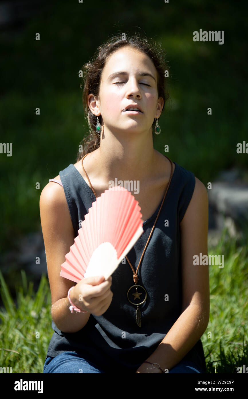 Chica adolescente con abanico sudando y pasando calor al sol Stock Photo