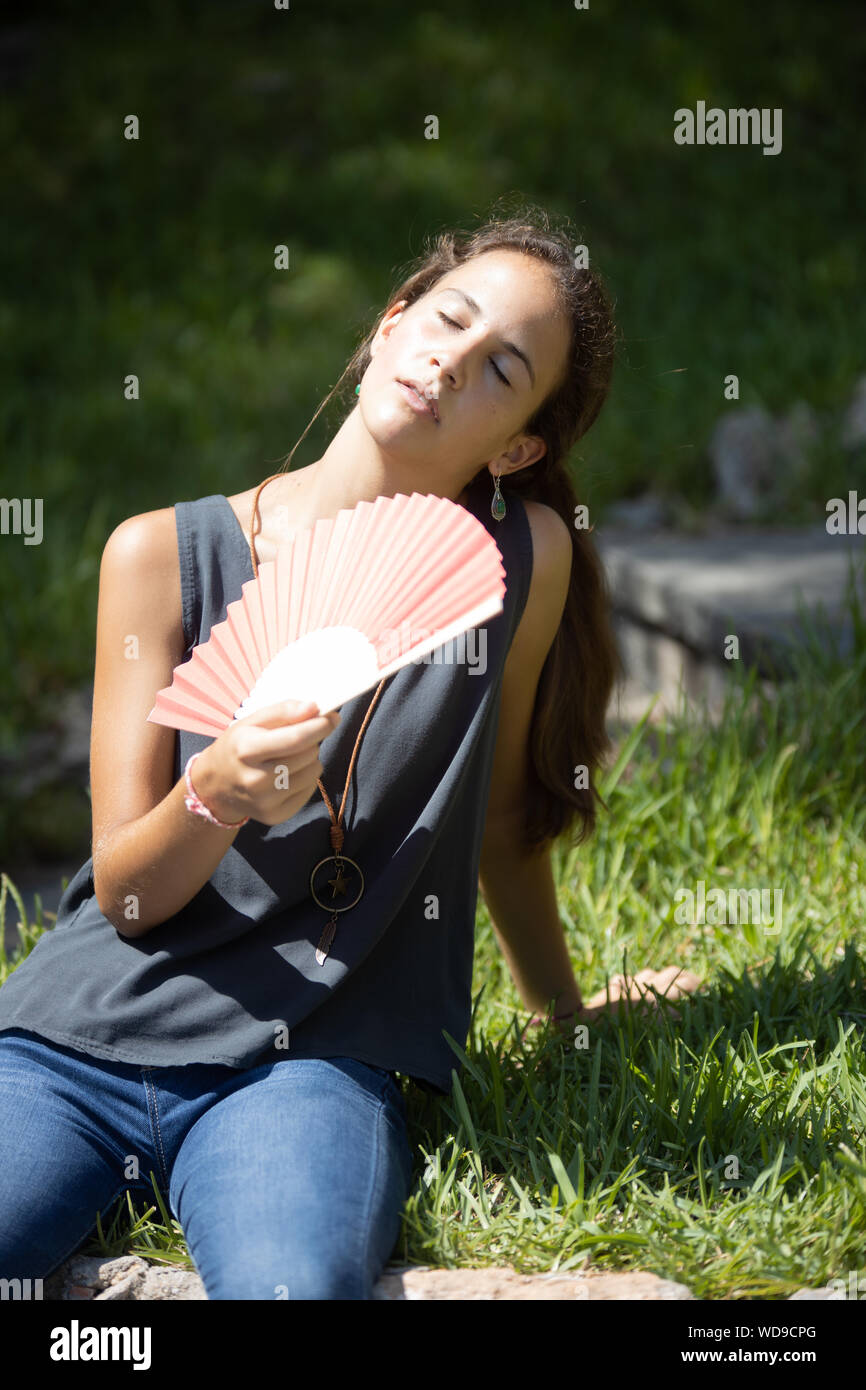 Chica adolescente con abanico sudando y pasando calor al sol Stock Photo