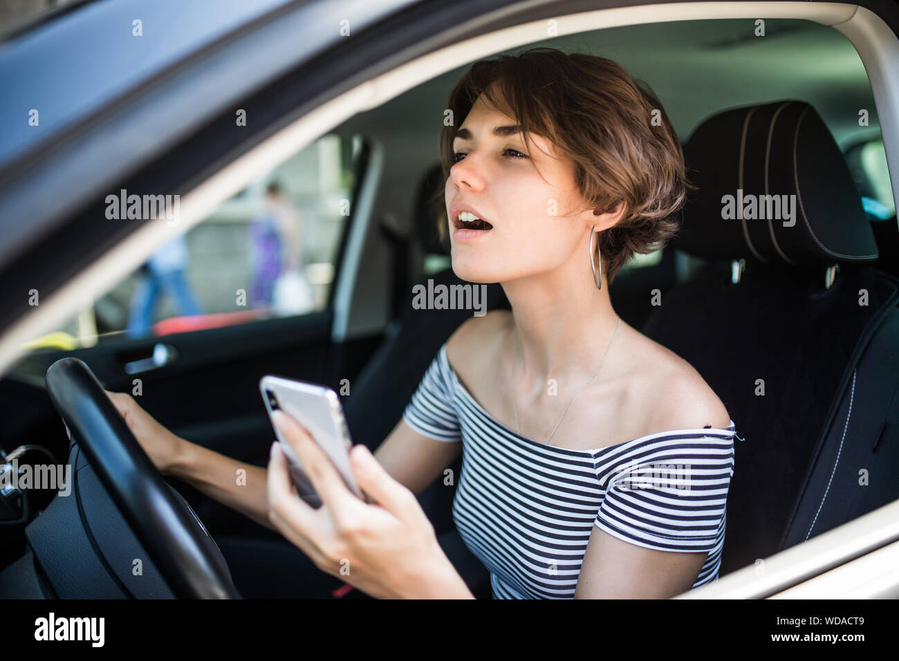 Closeup portrait, young woman driving in black car and checking her phone, annoyed by navigation gps system or bad text message or email, isolated out Stock Photo