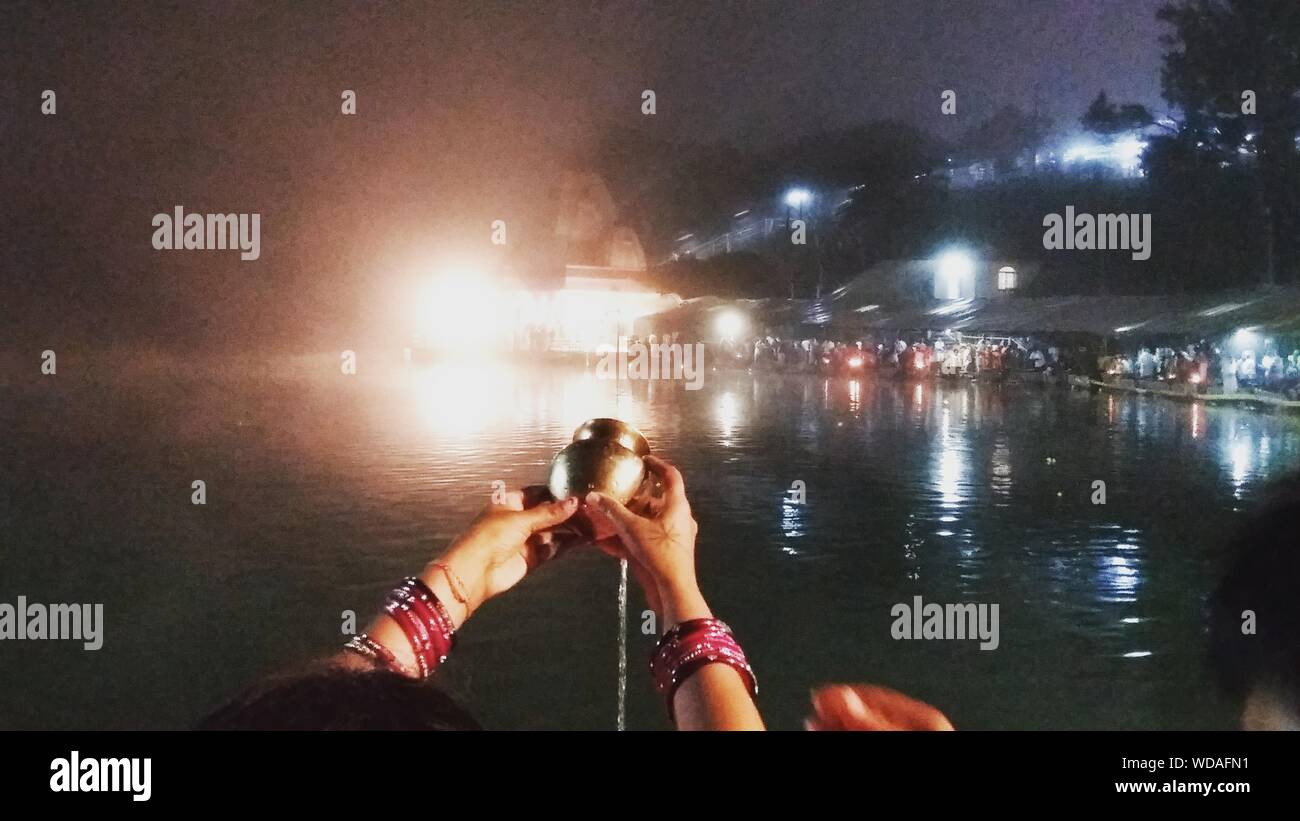 Cropped Image Of Woman Pouring Water In Ganga Talao From Lota At Night Stock Photo