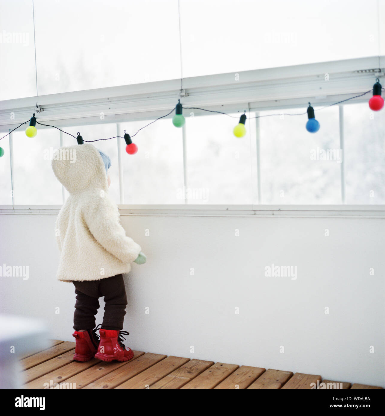 Rear view of child wearing warm clothes and looking out window Stock Photo