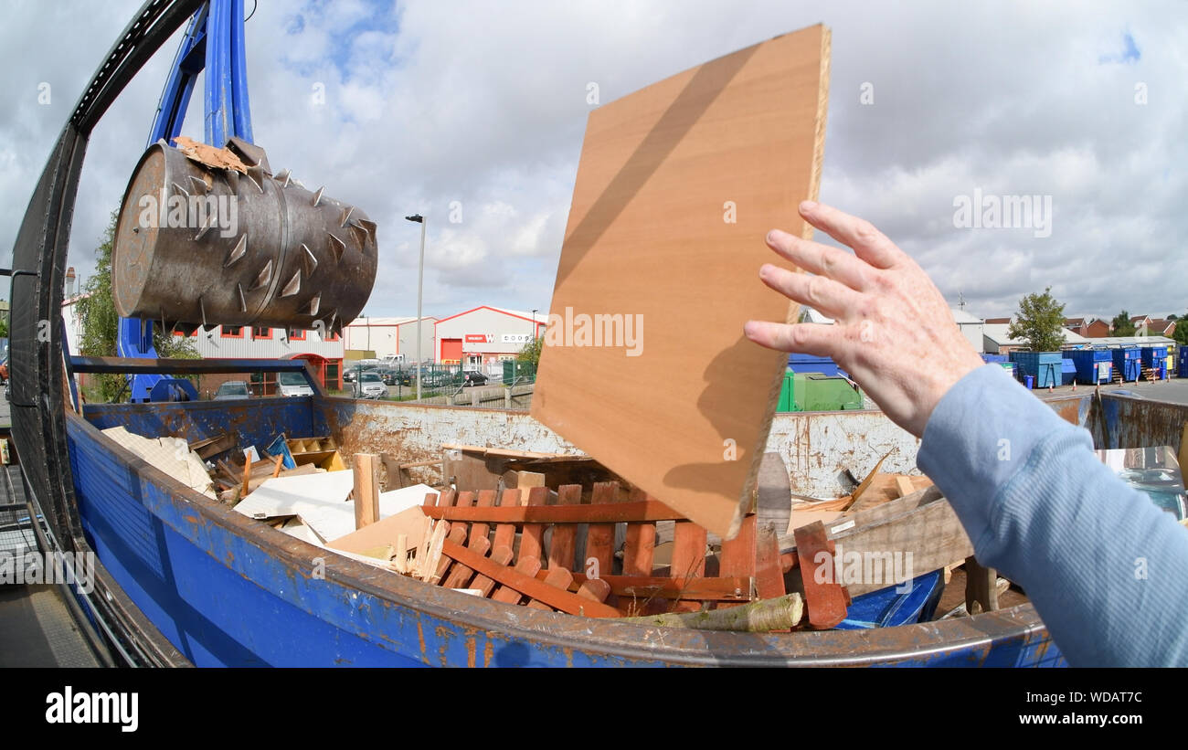 man throwing wood into skip for processing by hydraulic arm crushing
