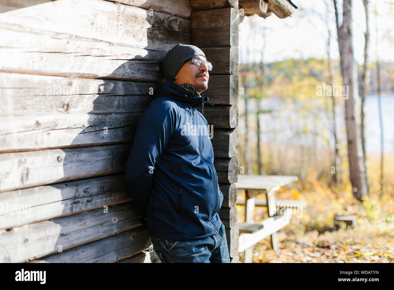Man wearing beanie and jacket leaning on log cabin Stock Photo