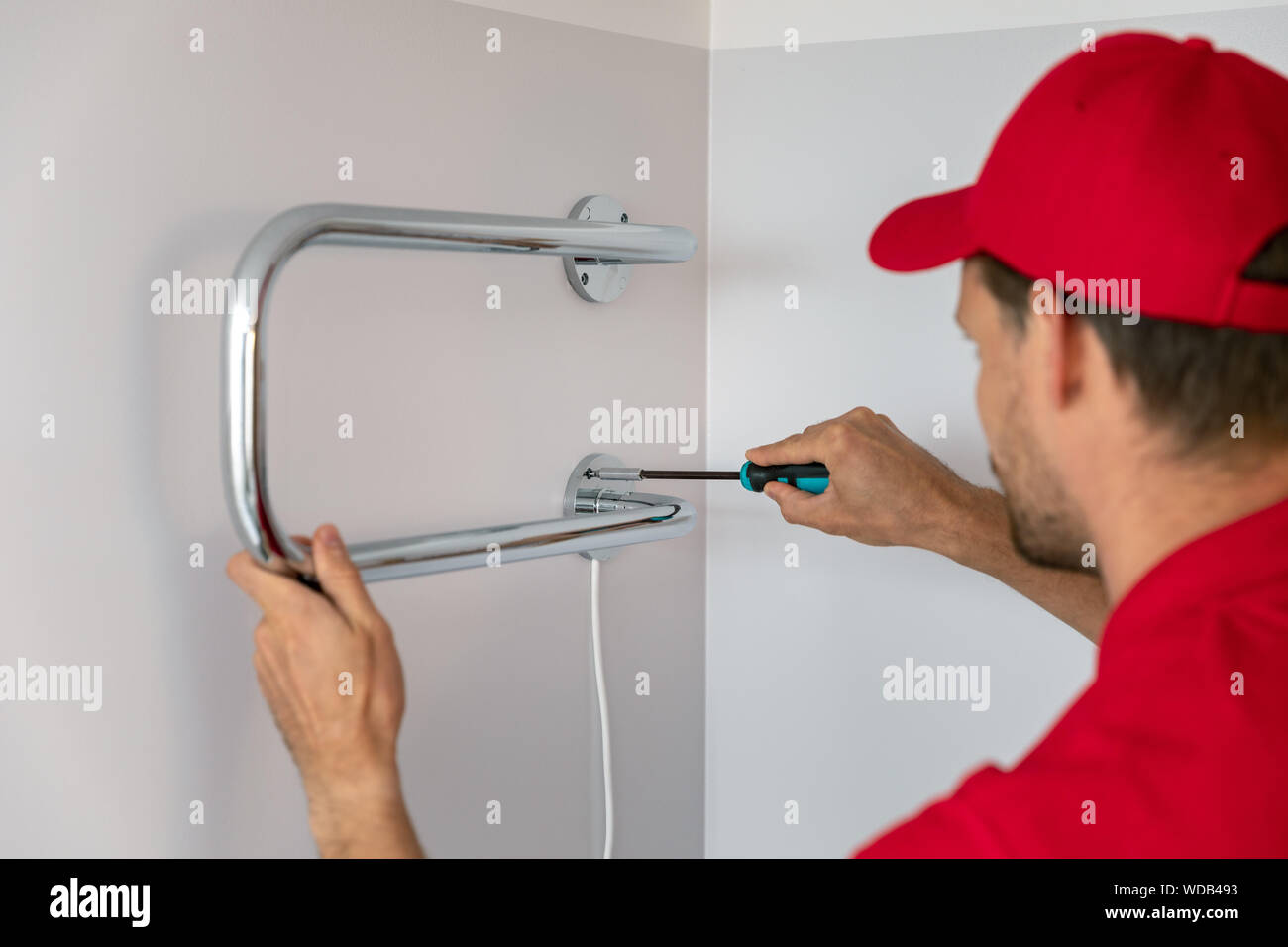 worker installing electric towel dryer on the bathroom wall Stock Photo