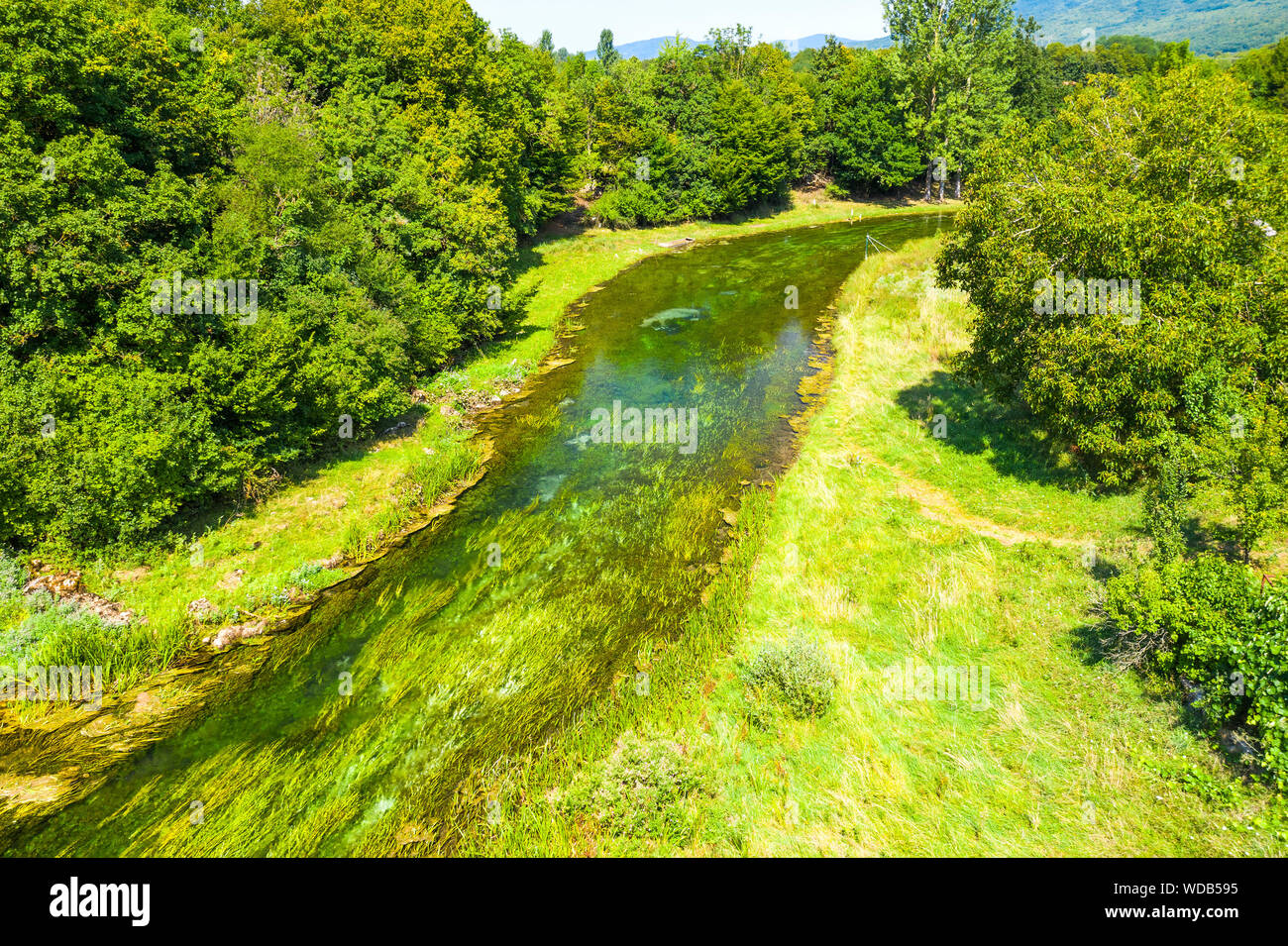 Beautiful Gacka river flowing between trees and fields, summer view, Lika region of Croatia