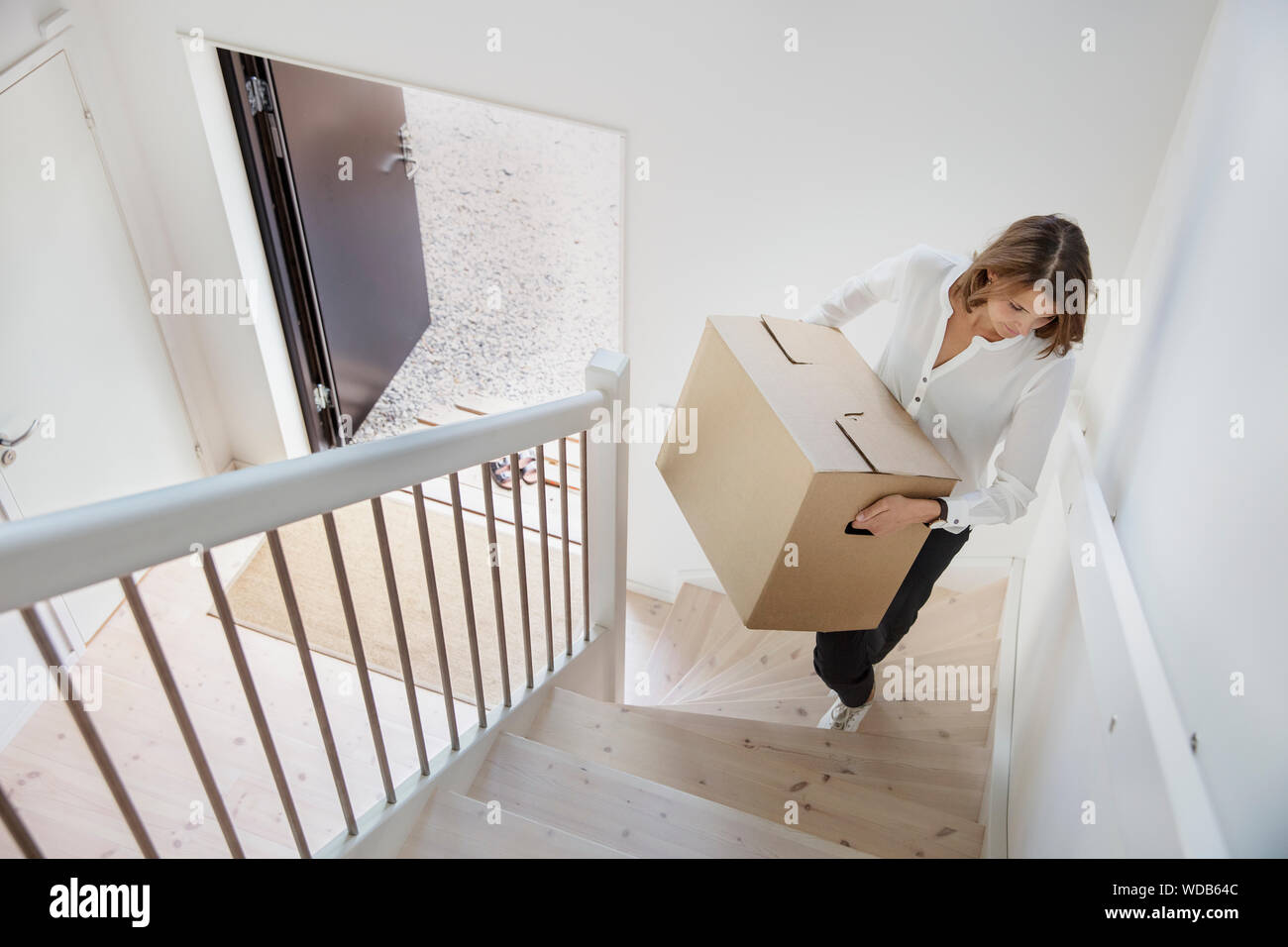 Woman carrying cardboard box up staircase Stock Photo Alamy