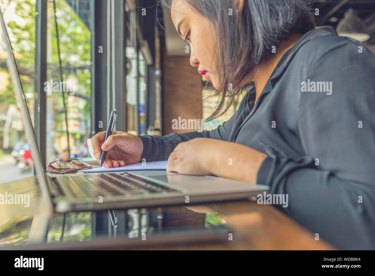Asian millennial working on laptop and writing notes Stock Photo