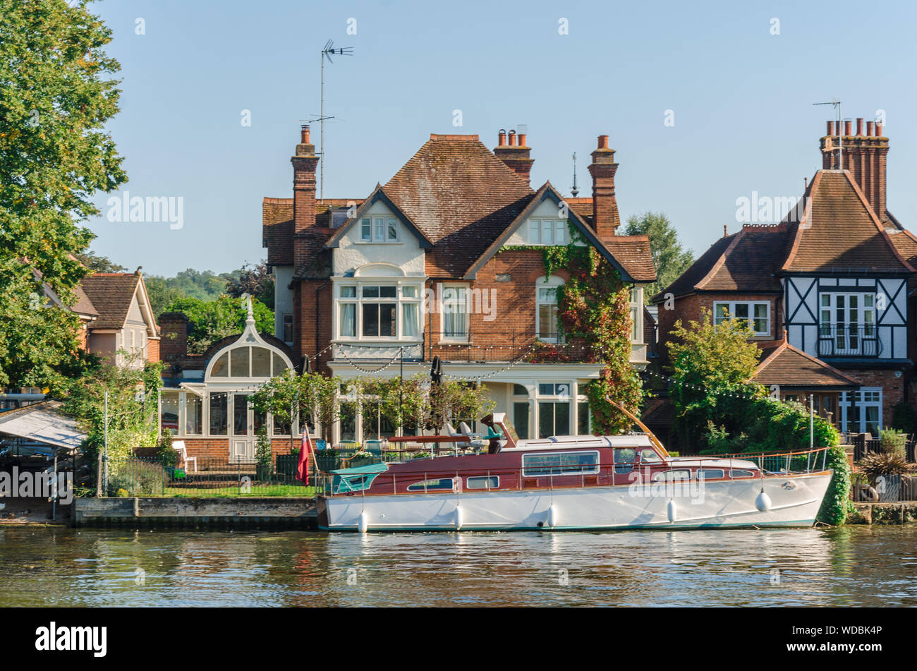 A boat in Marlow backs onto the River Thames and has a pleasure boat moored on the river at the bottom of the garden. Stock Photo