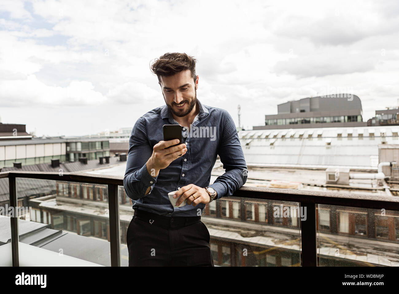 Young man looking at cell phone on balcony Stock Photo