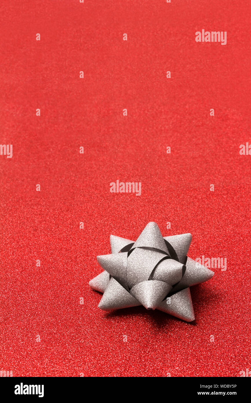 Silver gift bow on glitter red bachground with copy space. Stock Photo