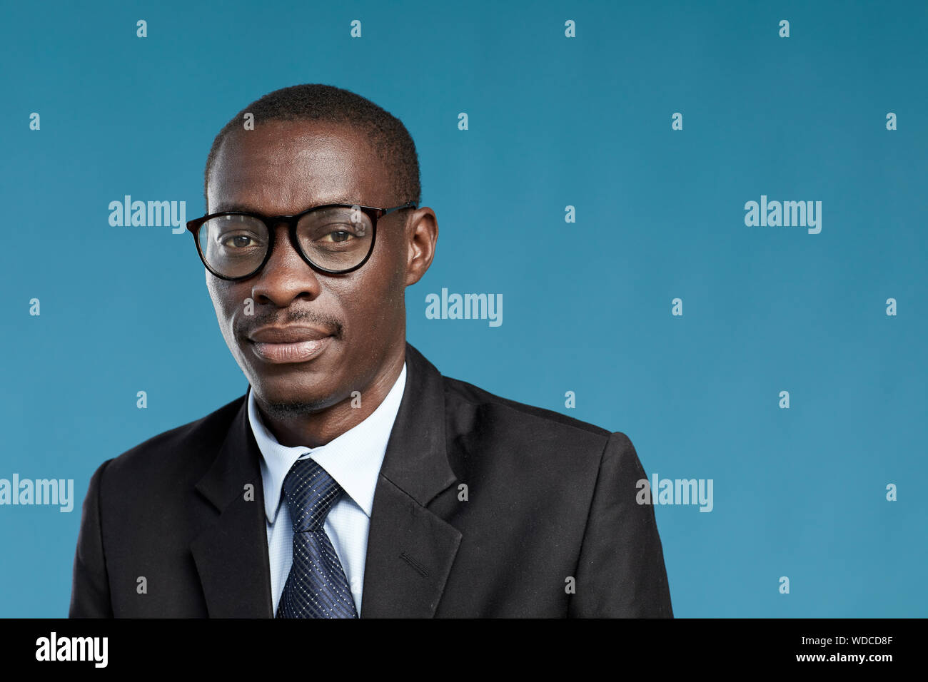 Portrait of young African businessman in eyeglasses and suit looking at camera isolated on blue background Stock Photo
