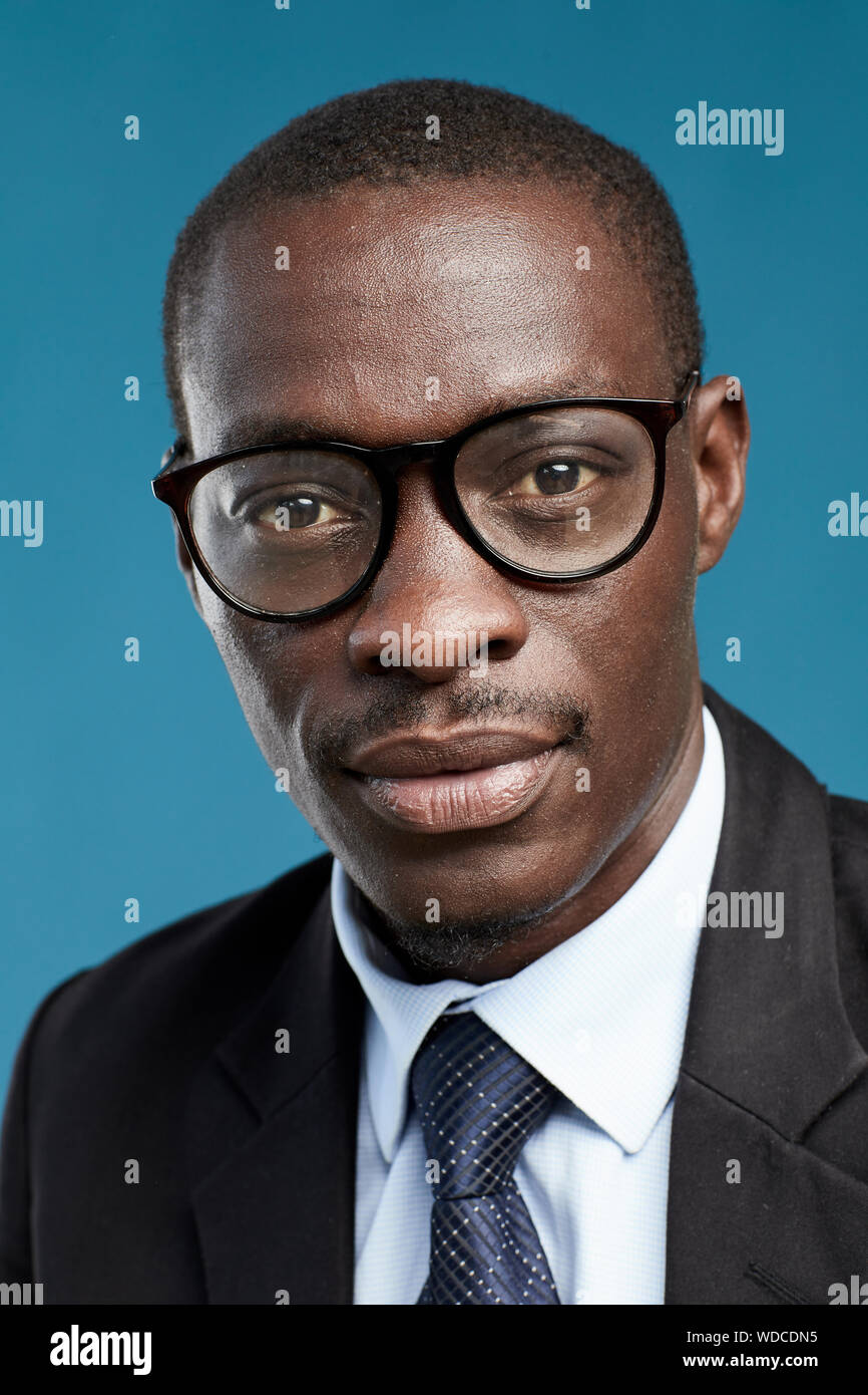 Close-up of African serious businessman wearing eyeglasses and suit looking at camera over blue background Stock Photo