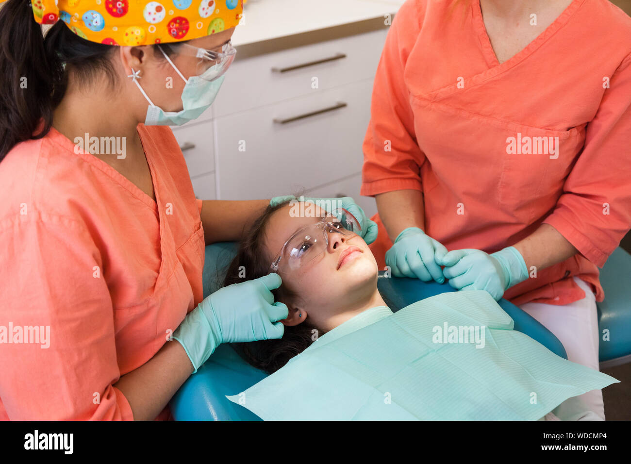 Pretty young girl a the dentist surgery for checkup with female dentist and assistant, putting on protective glasses Stock Photo