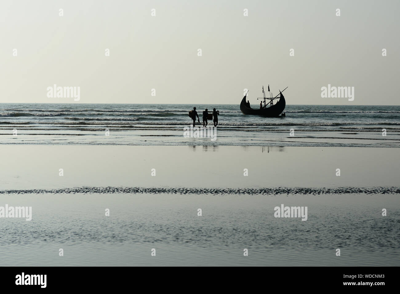 The fishermen are going to the traditional fishing boat (Sampan Boats) moored on the longest beach, Cox's Bazar in Bangladesh. Stock Photo