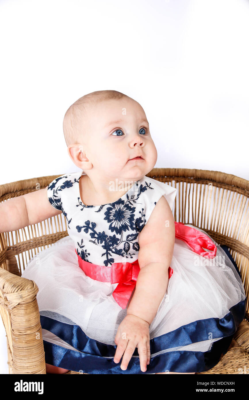 6 Months old baby girl in a cute dress sitting on a rattan chair Stock Photo