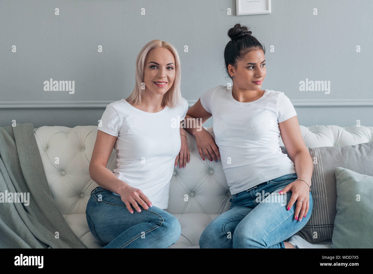 Two attractive girls dressed in casual style sitting on the couch in the room Stock Photo