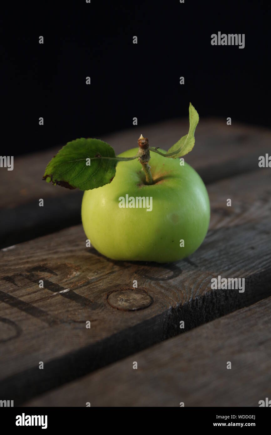 A healthy little green apple with a couple of leaves attached sitting on a wooden crate. Still life. Stock Photo