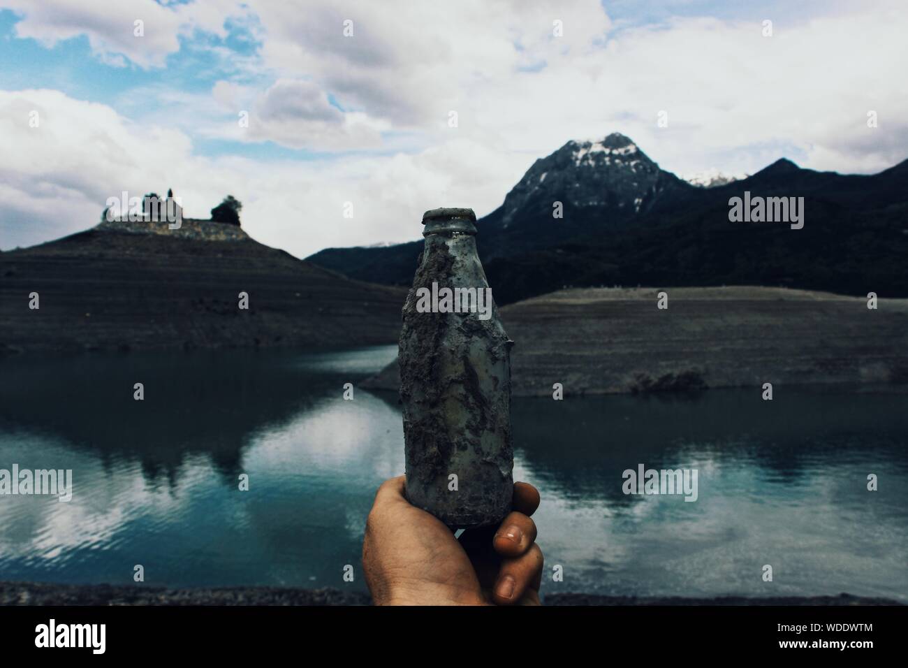 Person holding an old glass bottle covered in mud near the water with ...