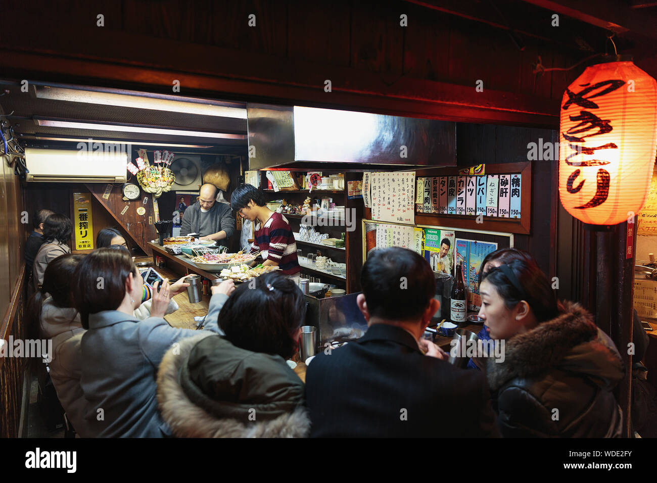 People enjoy drinks and street food inside a small pub in Omoide Yokocho alley. Stock Photo