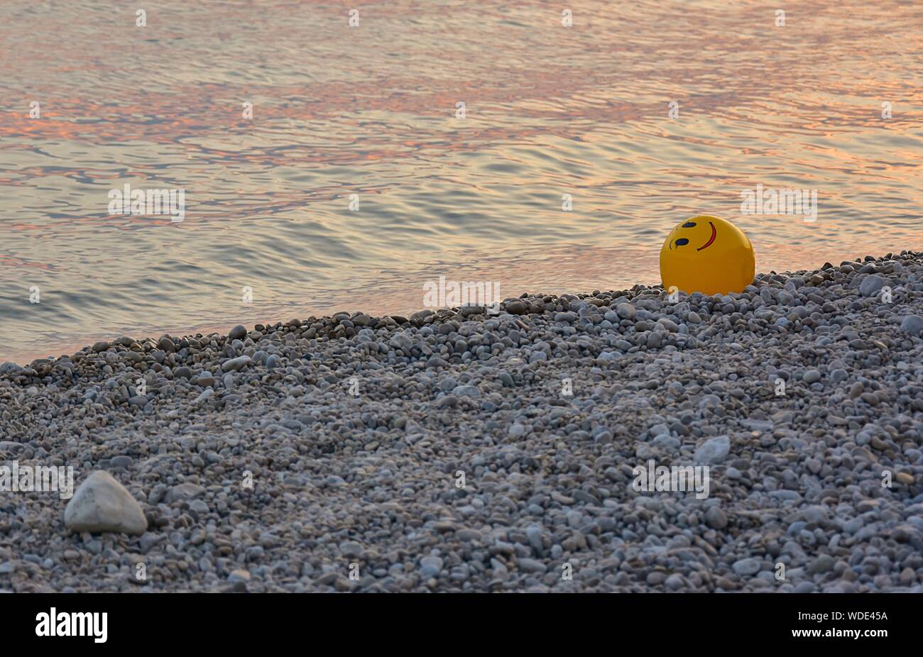 A yellow ball on a pebble beach at sunset. Ball with smiley face. Stock Photo