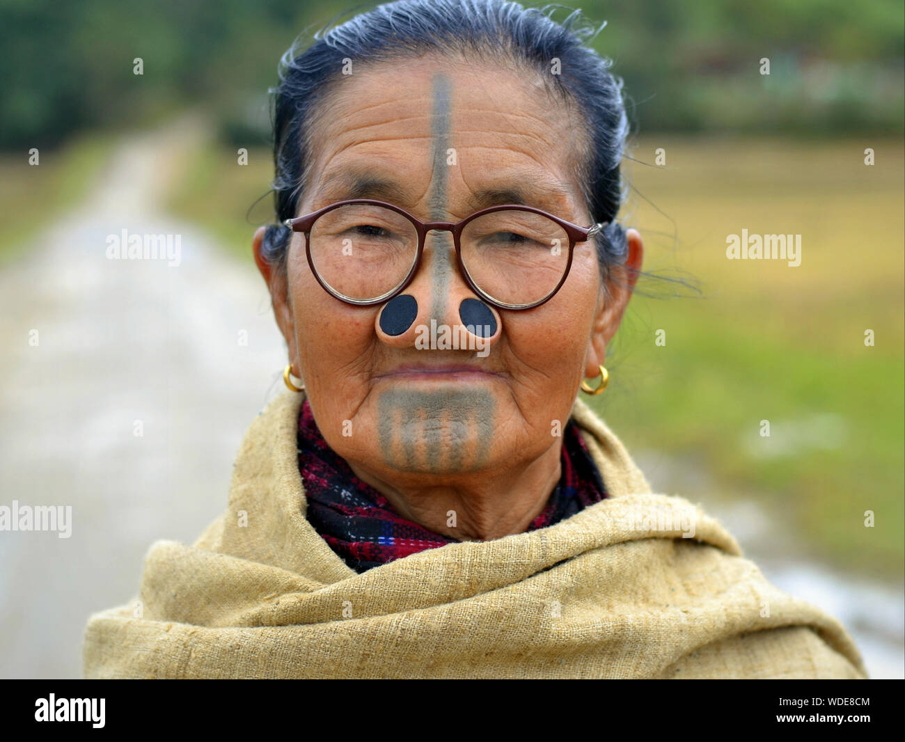 Elderly Indian Apatani tribal woman with black wooden nose plugs (yaping hullo) and distinctive tribal face tattoo poses for the camera. Stock Photo