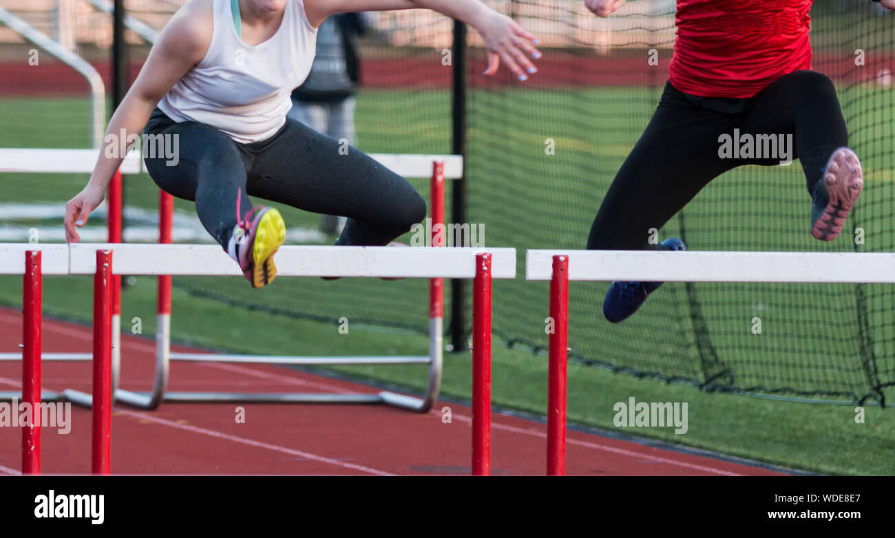 Two high school girls racing each other in the hurdles during a track
