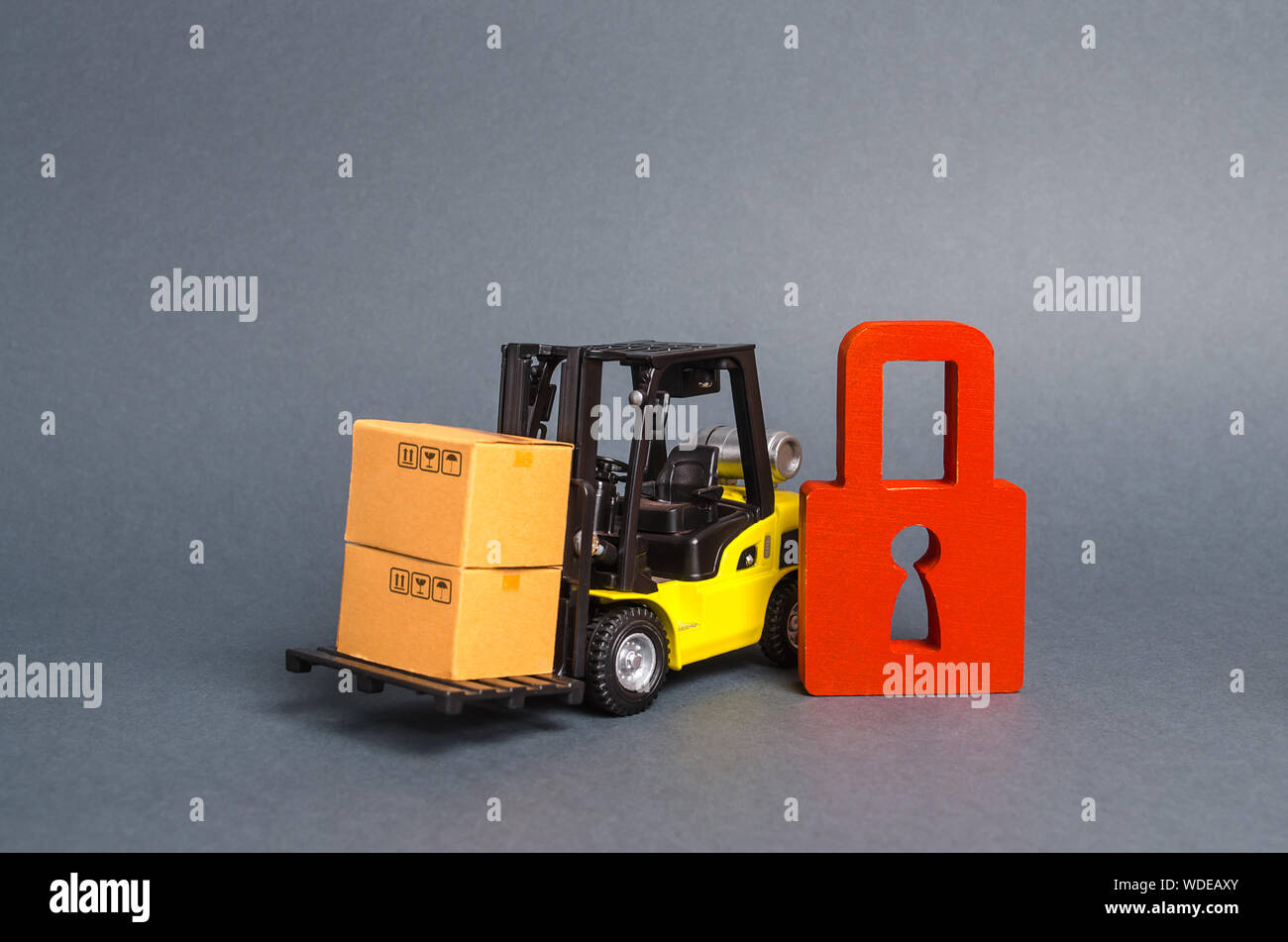 Forklift truck carries a cardboard box next to red padlock. Embargo, trade wars. No delivery. Restriction on the importation of goods, proprietary for Stock Photo