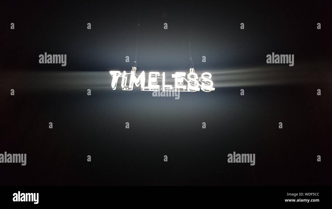 Low Angle View Of Illuminated Timeless Text Hanging Against Black Background Stock Photo