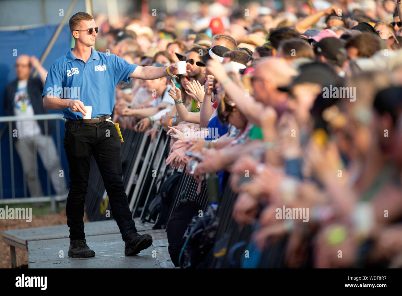 A Security Guard Hands Out Water To Fans Of Two Door Cinema Club