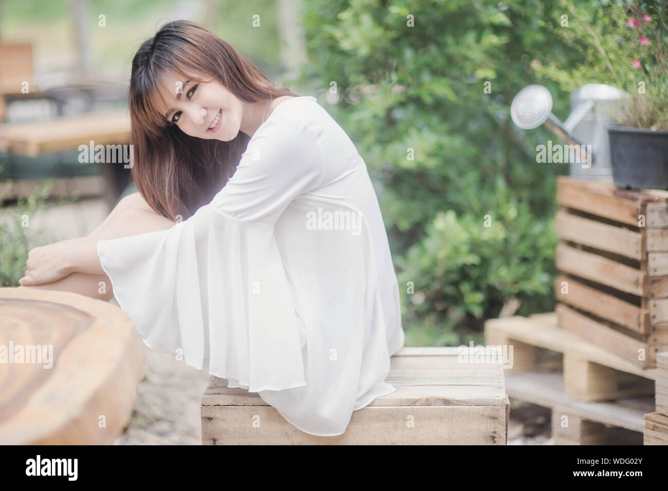 Young Woman Sitting On Crate Against Plants Stock Photo Alamy