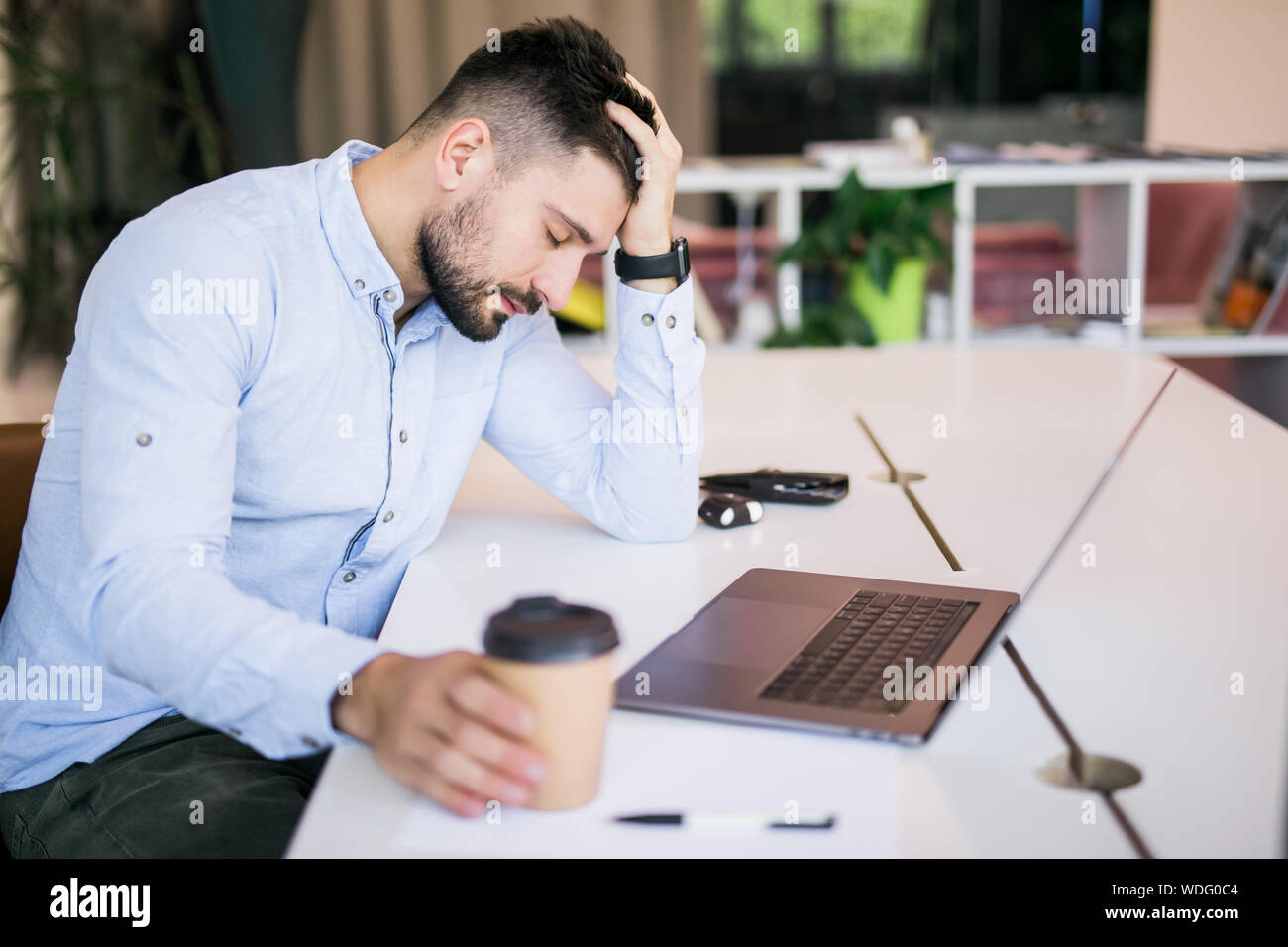 Young business man with fake eyes painted on paper stickers yawning at  workplace in office Stock Photo