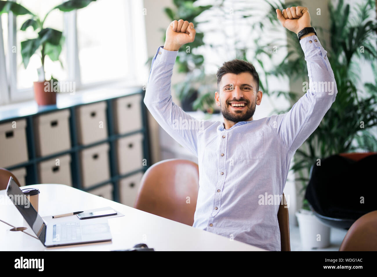 Young businessman celebrating his success with arms raised at his ...