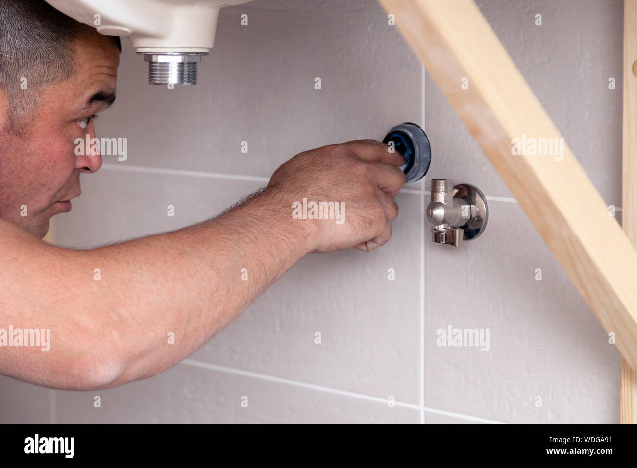 Closeup male plumber worker in blue denim uniform, overalls, fixing